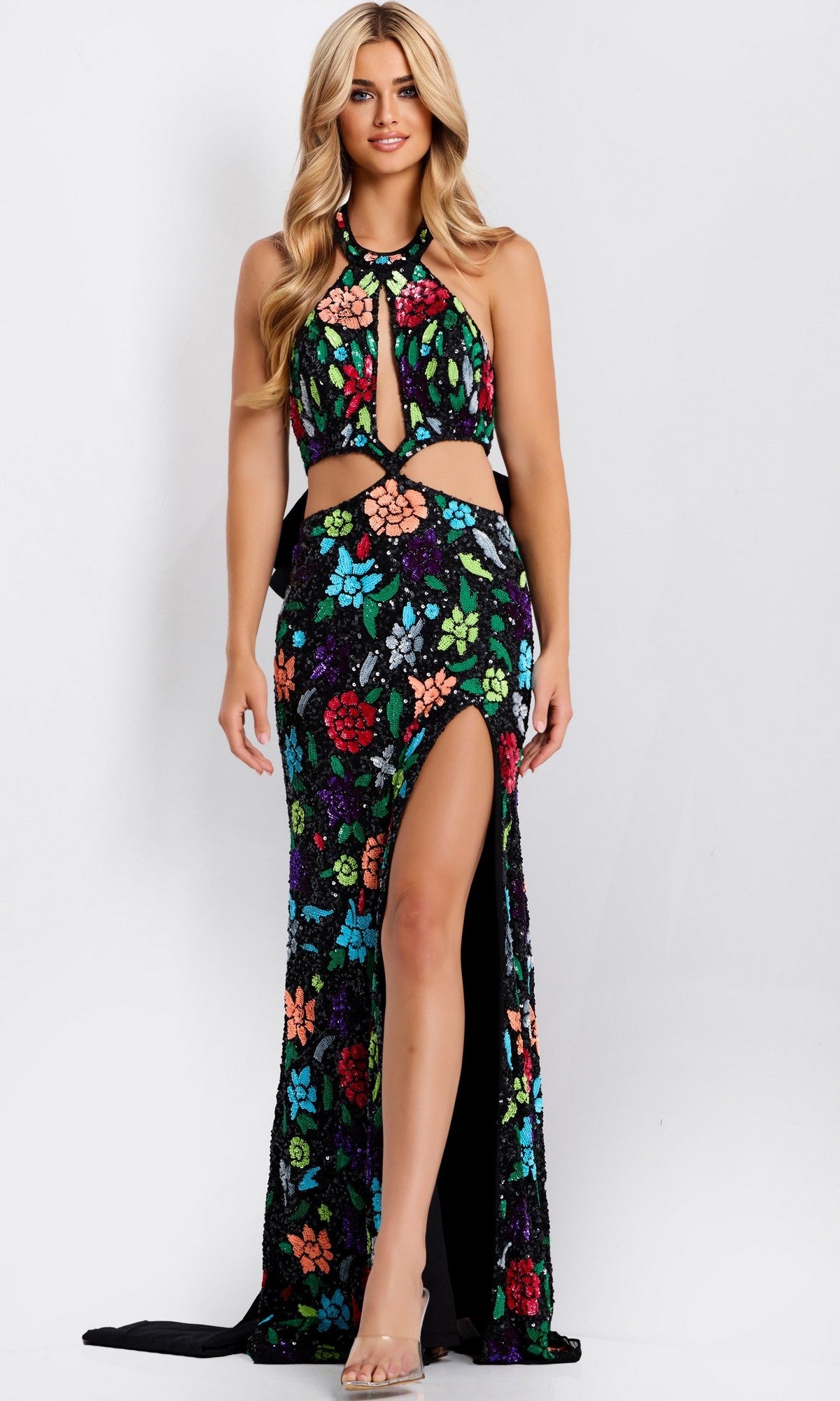 A woman models the Jovani 49251 long prom dress featuring a multicolored floral sequin design, halter neckline, high slit, and cut-out waist, paired with clear heels against a plain white background.